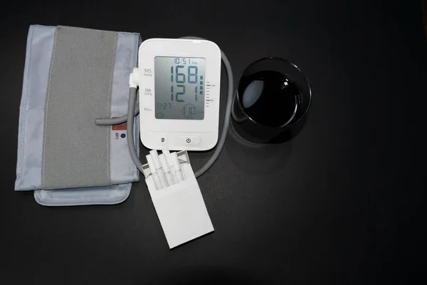 blood pressure and heart rate monitor high blood pressure and heart rate measurements. cigarettes and alcoholic drink on the side. unhealthy lifestyle. black background