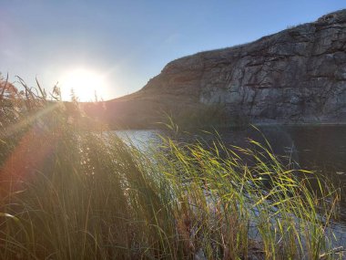 a quiet river among mighty and majestic rocks and black vegetation at sunset