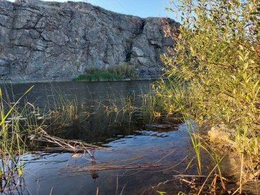 a quiet river surrounded by mighty rocks and green vegetation under a blue sky