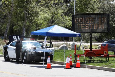 26 Mart 2020 'de Pacoima, Los Angeles, Kaliforniya, ABD' deki Hansen Baraj Parkı 'ndaki Coronavirus COVID-19 test merkezine giriş yapan bir Los Angeles polis memuru görülüyor..