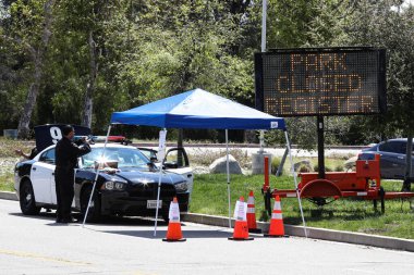 26 Mart 2020 'de Pacoima, Los Angeles, Kaliforniya, ABD' deki Hansen Baraj Parkı 'ndaki Coronavirus COVID-19 test merkezine giriş yapan bir Los Angeles polis memuru görülüyor..