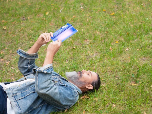 Zdjęcie mężczyzny w średnim wieku z książką w parku. Leży na trawie w parku i czyta książkę. Koncepcja detoksykacji cyfrowej. — Zdjęcie stockowe