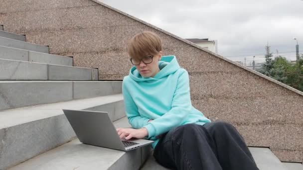 Молода жінка з коротким волоссям сидить на сходах з ноутбуком. Концепція онлайн-освіти . — стокове відео