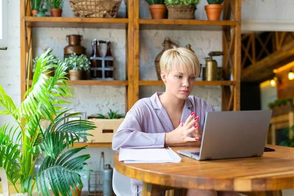 Mulher no pijama trabalha com documentos na frente de um monitor de laptop no interior da casa. — Fotografia de Stock