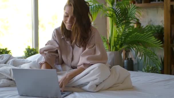 Mulher na frente de um monitor de laptop na cama. Freelance - fala sobre comunicação por vídeo e gestos ativos. — Vídeo de Stock