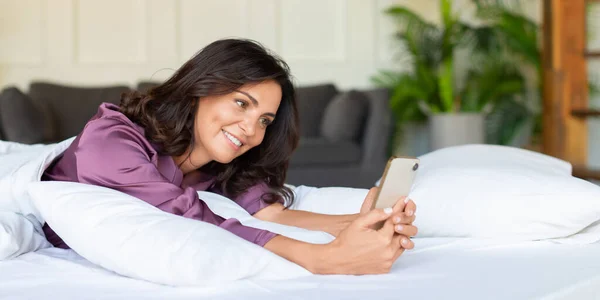 한 여자가 스마트폰을 들고 침대에 누워 있는 모습. 셰 이즈는 어색 함 이후 소셜 미디어를 점검 한다. 현대 과학 기술 개념. — 스톡 사진