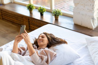 Yatağında akıllı telefonuyla gülümseyen kadın uyandı.,