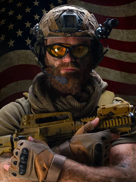 Portret van een Amerikaanse soldaat die rouwt om de gevallen vrienden tegen de achtergrond van de Amerikaanse vlag. Hij houdt zijn wapen vast en kijkt recht in de camera. Veteranen Memorial Day concept. — Stockfoto