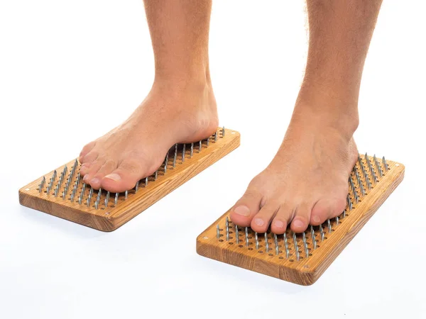 Male feet stand on a board with sharp nails over white background. Sadhus board - practice yoga. Pain, trials, health, relaxation, cognition. Close-up.