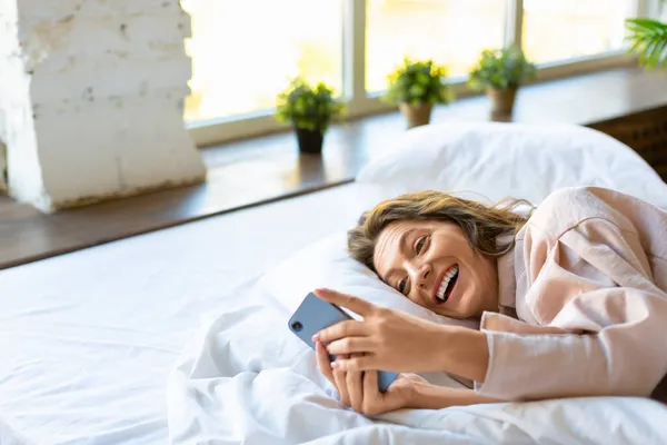 Wanita dengan smartphone di tempat tidur. Dia punya kabar baik.. — Stok Foto