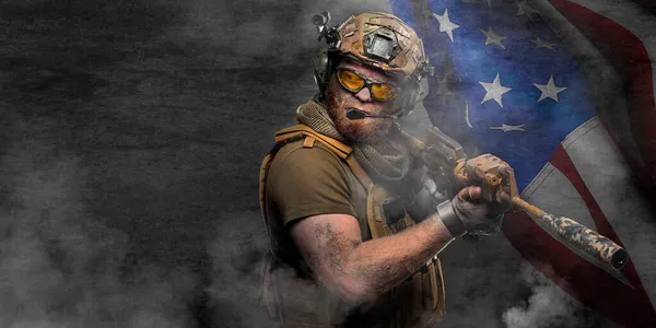 Профессиональный солдат спецназа, во время спецоперации в дыму на темно-бетонной стене и фоне флага США - он защищает флаг. Фото с копировальным пространством - формат 2x1. — стоковое фото
