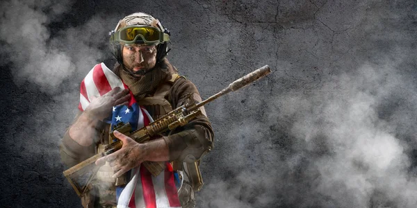 Um soldado de infantaria americano está contra o fundo de uma parede de concreto com uma bandeira em seus ombros. Conceito do dia da lembrança de veteranos. — Fotografia de Stock