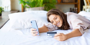 Mutlu, gülümseyen bir kadın mobil bir uygulama aracılığıyla sipariş veriyor. Çevrimiçi alımlar için kart numarasını çeviriyor. Biçim fotoğrafı 2x1.