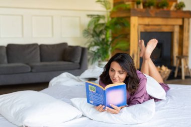 Dijital detoks konsepti. Orta yaşlı bir kadın kitap okurken yatakta dinleniyor..