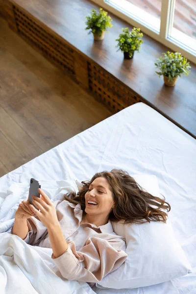 침대에 스마트폰을 가지고 있는 35 세 여성의 수직 사진. 좋은 소식 이 있어. — 스톡 사진
