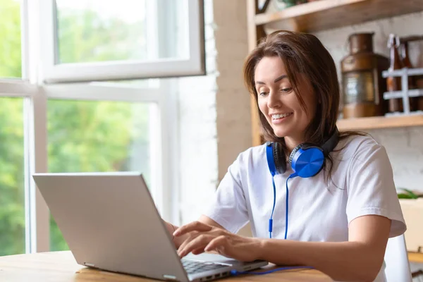 Mulher sorridente trabalhando em casa na frente de um monitor de laptop. Ela ergueu o dedo para indicar a importância da ideia. Formato foto 2x1. — Fotografia de Stock