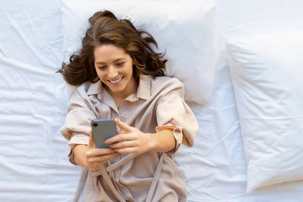 Vue du dessus d'une femme de 35 ans avec smartphone au lit. Elle a une bonne nouvelle.. — Photo