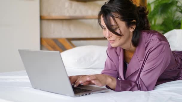 Medelålders kvinna framför en laptop monitor i sängen. Frilans - hon har chatt online. — Stockvideo