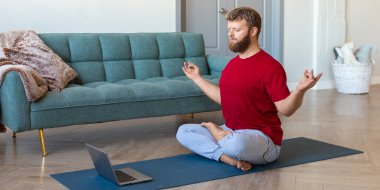 Ruh sağlığı konsepti. Orta yaşlı bir adamın online yoga dersi alırken çekilmiş fotoğrafı. Dizüstü bilgisayarın önünde meditasyon yapıyor..