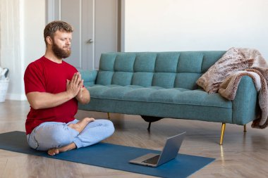 Akıl sağlığı konsepti. Orta yaşlı bir adam online yoga dersi alıyor. Dizüstü bilgisayarın önünde meditasyon yapıyor..