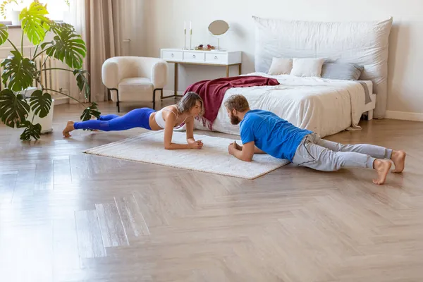 Een stel van middelbare leeftijd dat thuis traint. Plankpositie. Het concept van een gezonde levensstijl en het in vorm houden na de leeftijd van 40 jaar. — Stockfoto