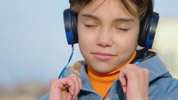Уверенная девушка-подросток слушает рэп-музыку через синие беспроводные наушники и онлайн-приложение для смартфонов на открытом воздухе. — стоковое видео