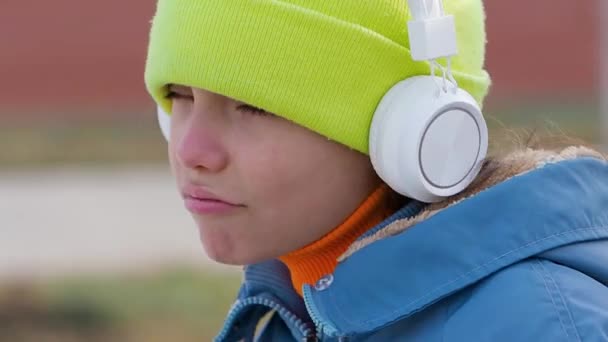 Overmoedig en brutaal tienermeisje luisteren naar rapmuziek via witte draadloze hoofdtelefoon en online smartphone app buiten. — Stockvideo