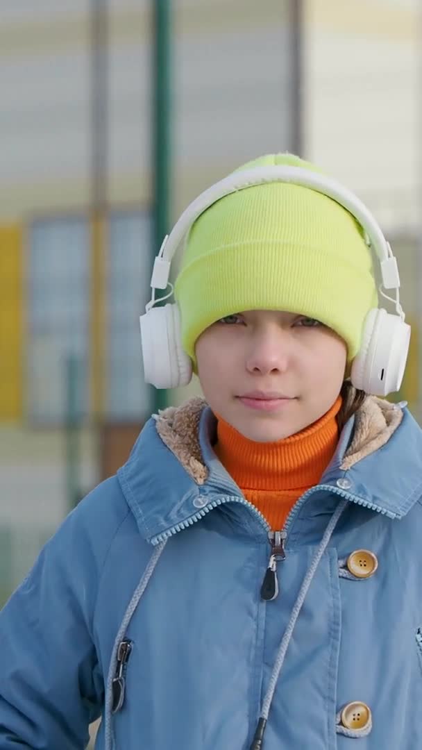 Pionowe wideo nastolatki słuchającej muzyki za pośrednictwem bezprzewodowych słuchawek i aplikacji online na smartfona outdoor. — Wideo stockowe