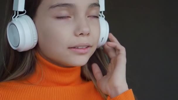 Teenager girl listening to the music via wireless headphones and online smartphone app indoor. Close-up portrait. — Stock Video