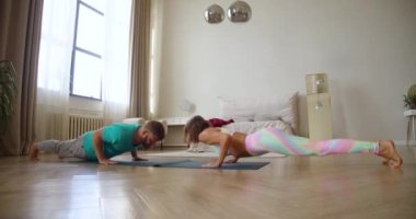 Orta yaşlı bir çift evde birbirlerinin önünde yoga egzersizleri yapıyor. Yukarı doğru köpek egzersizi yapıyorlar. 4K görüntü.