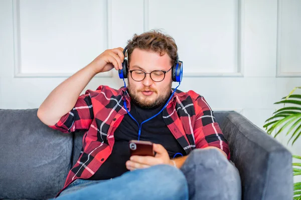 Evde çalışan, kulaklıklı ve akıllı telefonlu genç bir adamın fotoğrafı. O, akıllı telefonlar için çevrimiçi uygulama üzerinden müzik dinliyor.. — Stok fotoğraf