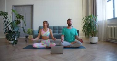 Orta yaşlı bir çift evde yoga dersi alarak meditasyon yapıyor. 4K görüntü.