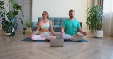 Orta yaşlı bir çift evde yoga dersi alarak meditasyon yapıyor. 4K yavaş çekim. Kamera insanlardan uzaklaşır.