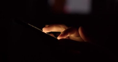 Karanlıkta akıllı telefonu olan bir kadın eli. Kadın resimleri izliyor ve kendini akıllı telefondan ayıramıyor. Dijital bağımlılık kavramı.