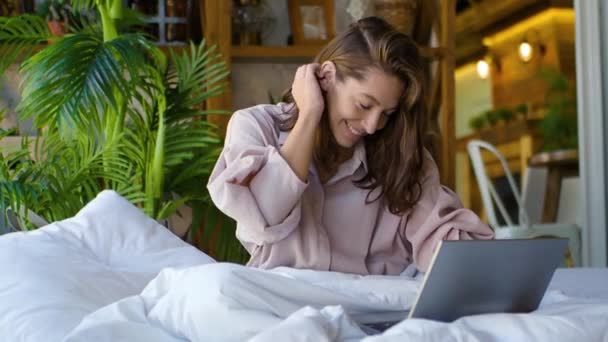 Mujer de 35 años delante de un monitor portátil en la cama. Freelance - habla sobre comunicación por vídeo y gestos activos. — Vídeos de Stock