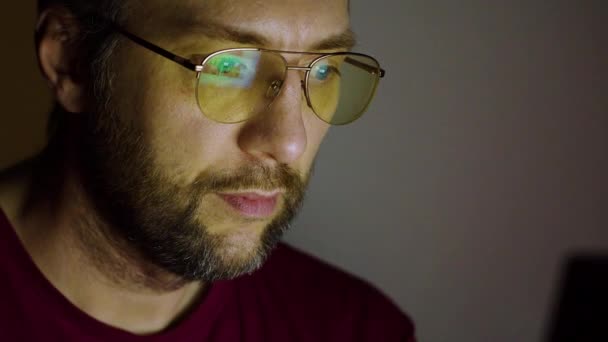 Das Gesicht eines Mannes mittleren Alters - er arbeitet nachts zu Hause vor einem Computermonitor. Überarbeitetes Konzept. FHD-Filmmaterial. — Stockvideo