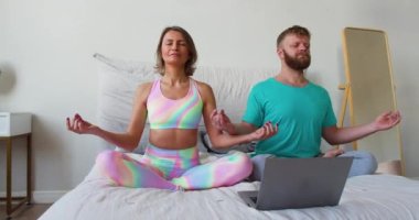 Orta yaşlı bir çift online bir akıl hocasının rehberliğinde dizüstü bilgisayar monitörünün önünde meditasyon yapıyor. 4K görüntü.