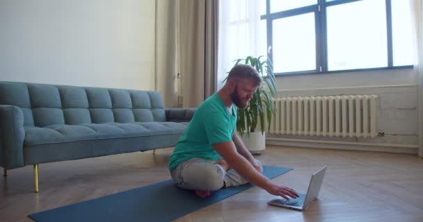 オンラインヨガクラスを受講している中年男性の写真 彼はノートパソコンのモニターの前の床に座って瞑想している 4K映像 — ストック動画