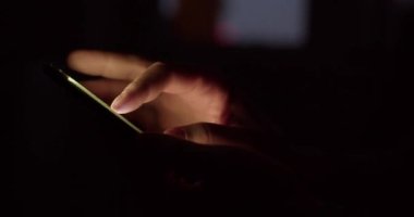 Karanlıkta akıllı telefonu olan bir erkek eli. Adam resimlere bakıyor ve kendini akıllı telefondan ayıramıyor. Dijital bağımlılık kavramı.