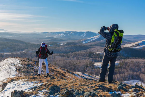 Homme d'âge moyen prend une photo de sa femme avec un smartphone tout en randonnée dans les montagnes alpines d'hiver au lever du soleil. — Photo
