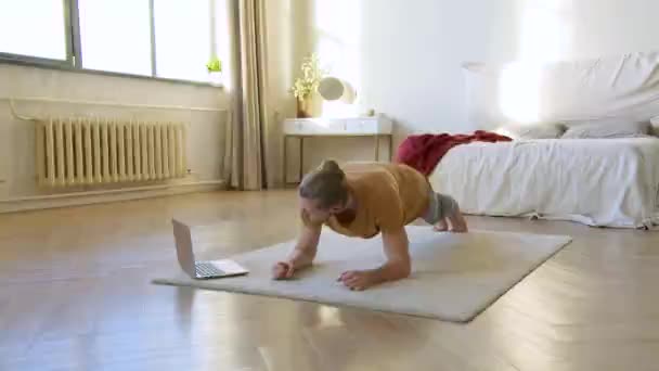 Junger Mann vor dem Laptop-Monitor bei der Plank-Übung. Heimtraining. Er folgt der Anleitung seines Online-Trainers. — Stockvideo