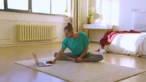Trening jogi online w domu. Młody człowiek wybiera kurs w internecie i rozciąga plecy.. — Wideo stockowe