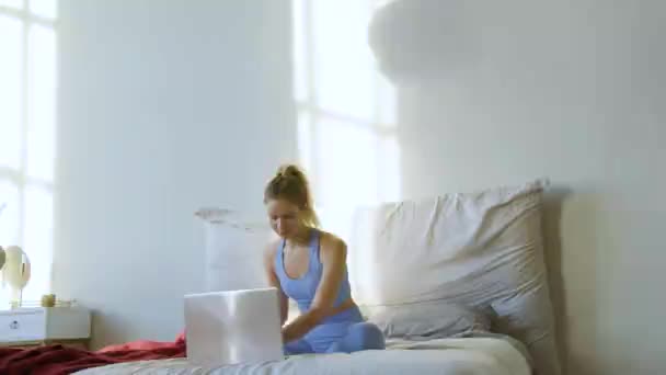 Online yoga workout online thuis. Een jonge vrouw kiest een tutorial op het internet en mediteert op het bed. — Stockvideo