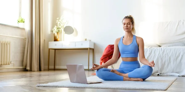 Evde online yoga çalışması. Genç bir kadın, bir bilgisayar ekranı önünde online bir eğitmenin rehberliği altında meditasyon yapıyor. Biçim fotoğrafı 2x1. — Stok fotoğraf