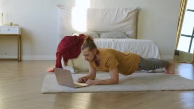 Genç adam dizüstü bilgisayar monitörünün önünde tahta pozisyonunda. Evde çevrimiçi çalışma.