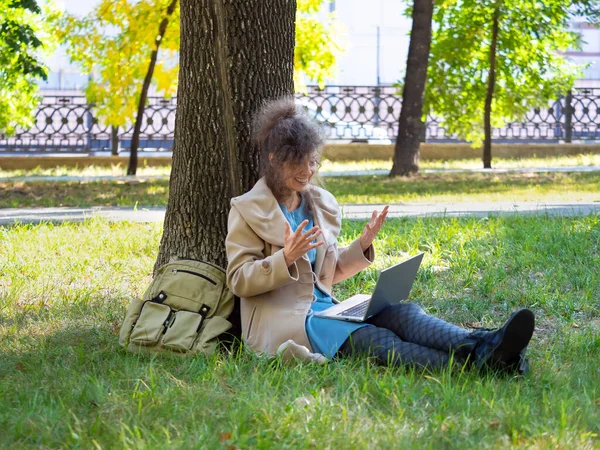 Uśmiechnięta kobieta w średnim wieku z laptopem w parku miejskim - wideo połączenie online. — Zdjęcie stockowe