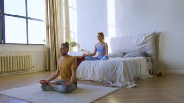 Genç çift evlerinde meditasyon yapıyor yatak odasında. Yoga pratiği. 4K görüntü.