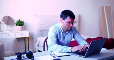 Evde dizüstü bilgisayarın önünde yorgun bir adam var. Serbest çalışan aşırı çalışma konsepti.