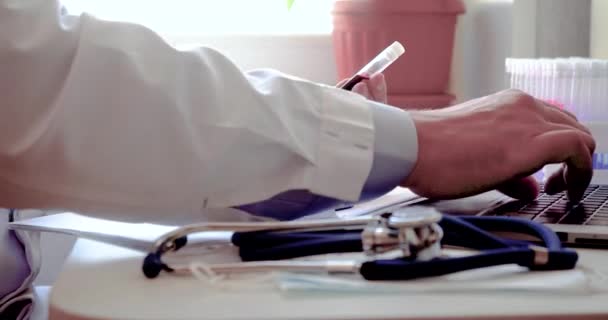 Doctor works with blood sample - he is typing a report on the latest vaccine on a laptop. — Stockvideo