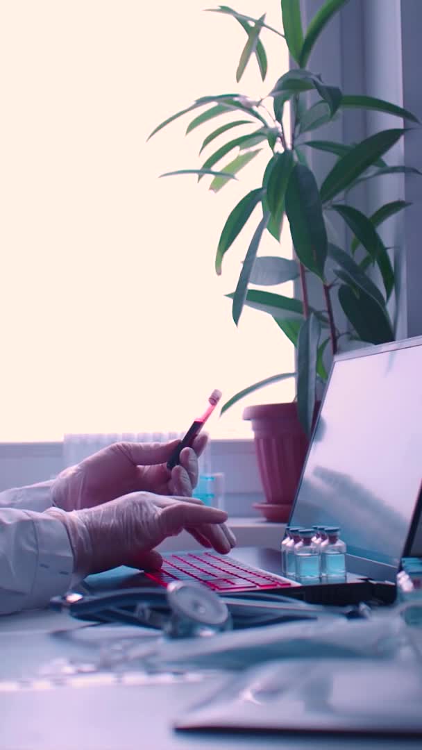 Ερευνητής γιατρός εργάζεται με δείγμα αίματος - δακτυλογραφεί μια έκθεση σχετικά με το τελευταίο εμβόλιο σε ένα φορητό υπολογιστή. Κάθετη βίντεο. — Αρχείο Βίντεο
